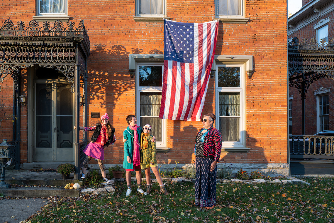People wearing Halloween costumes pose in front of an American flag and an old house in the historic neighborhood, before the 2020 United States presidential election