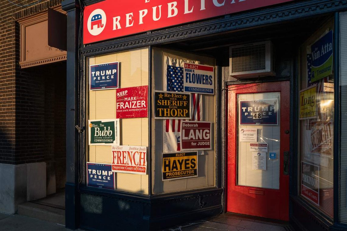 Political signs and an American flag displayed in the office window illuminated by evening light, before the 2020 United States presidential election