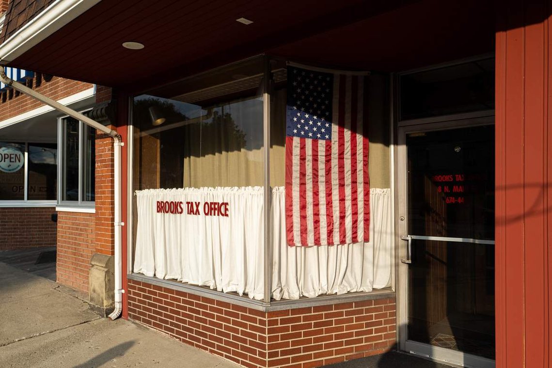An American flag illuminated by evening light displayed in the window of a local office in a small town, before the 2020 United States presidential election