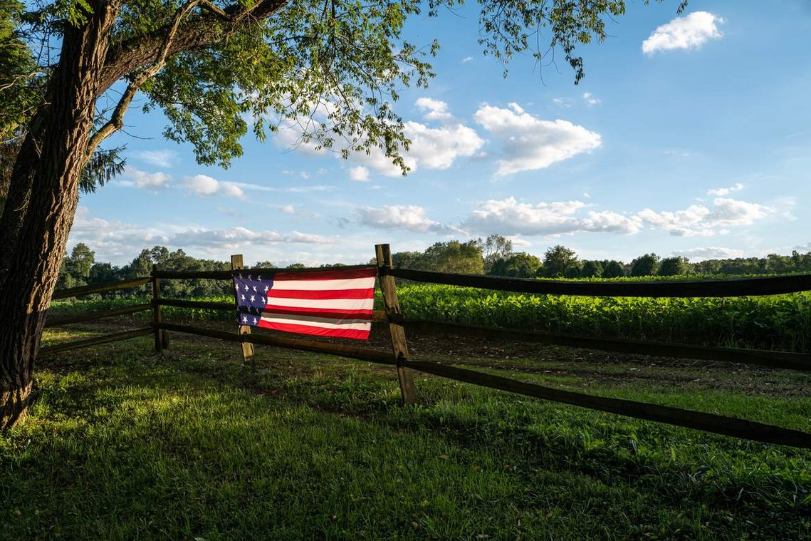 An American flag illuminated by evening light hanging on a fence in the idyllic countryside, before the 2020 United States presidential election 