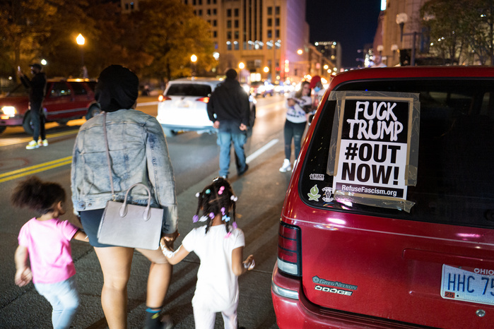 A car with anti-Trump sign parked on a street during celebrations of Biden victory in the 2020 United States presidential election, a mother and two daughters walk by it