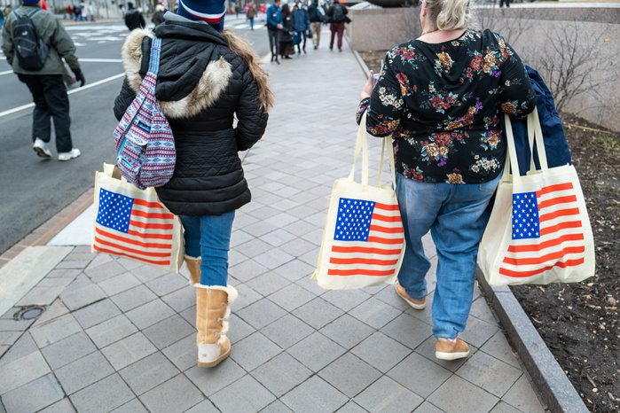 A mother and a daughter carrying American flag canvas totes on a street
