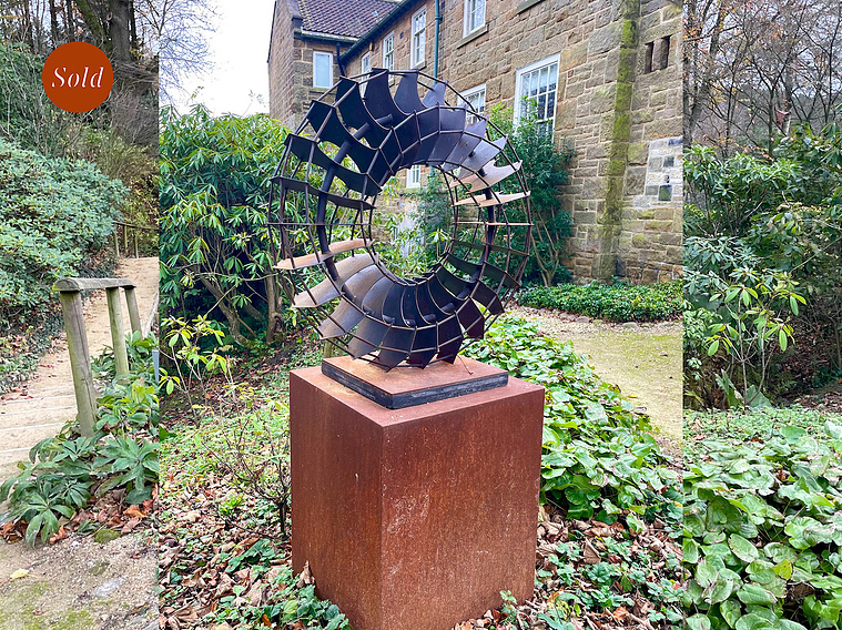 The black Vertebreath sculpture, sits on a corten steel plinth in a sculpture garden.
