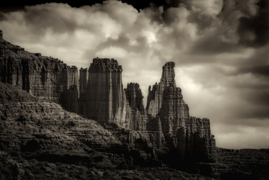 Dramatic light and shadow carve out the towering spires of Fisher Towers near Moab, Utah, as storm clouds gather above the sculpted sandstone formations—ancient monuments standing watch over the desert.