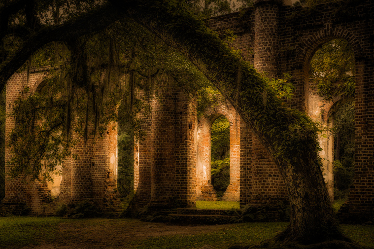 The brick columns of the Old Sheldon Church ruins rise hauntingly among moss-draped oaks in Yemassee, SC, bathed in soft, golden light that adds a timeless, reverent mood to the historic site.