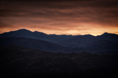 Layers of ridges fade into the distance at dawn in Great Smoky Mountains National Park, as a warm orange glow spreads across the sky, casting soft light over the dark, rolling silhouettes of the mountains.