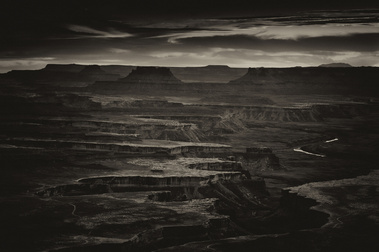 An early morning view from Canyonlands National Park reveals a labyrinth of shadowed mesas and deep canyons, with the winding Green River catching the first light beneath a brooding desert sky.