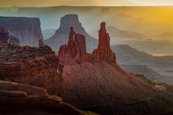 Sunrise bathes the towering spires of Canyonlands National Park, Utah, in golden light, casting long shadows across the layered desert landscape and revealing the park’s dramatic red rock formations in breathtaking detail.