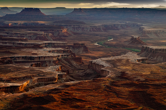 The Green River winds through a maze of layered red rock canyons in Canyonlands National Park, Utah, as the soft twilight casts warm highlights and deep shadows across the rugged desert landscape.