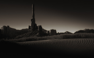 First light brushes the rippled desert sands and the towering spire of Totem Pole in Monument Valley, casting long shadows across the iconic landscape and awakening the silence of the Navajo Nation.