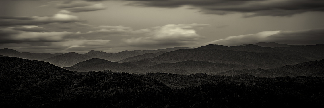 Rolling ridges fade into the distance under brooding skies in this moody dusk panorama of the Great Smoky Mountains National Park, where soft light and drifting clouds evoke a quiet, timeless atmosphere.