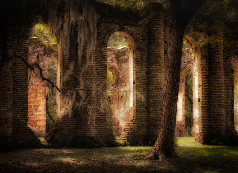 The brick columns of the Old Sheldon Church ruins rise hauntingly among moss-draped oaks in Yemassee, SC, bathed in soft, golden light that adds a timeless, reverent mood to the historic site.