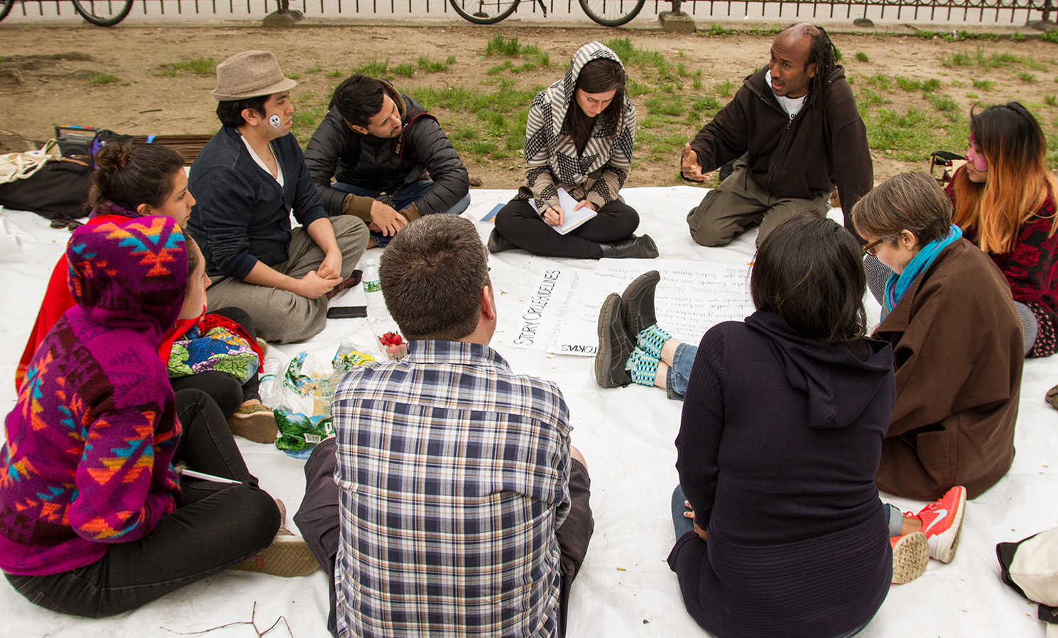 story circle of 10 community residents seated on blanket in park