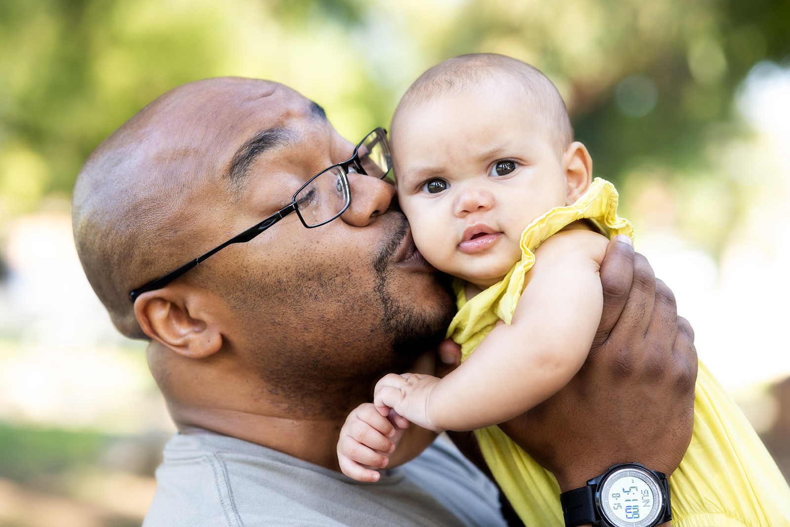 Family portrait of a black father kissing his mixed baby girl in Irvine Regional Park, CA