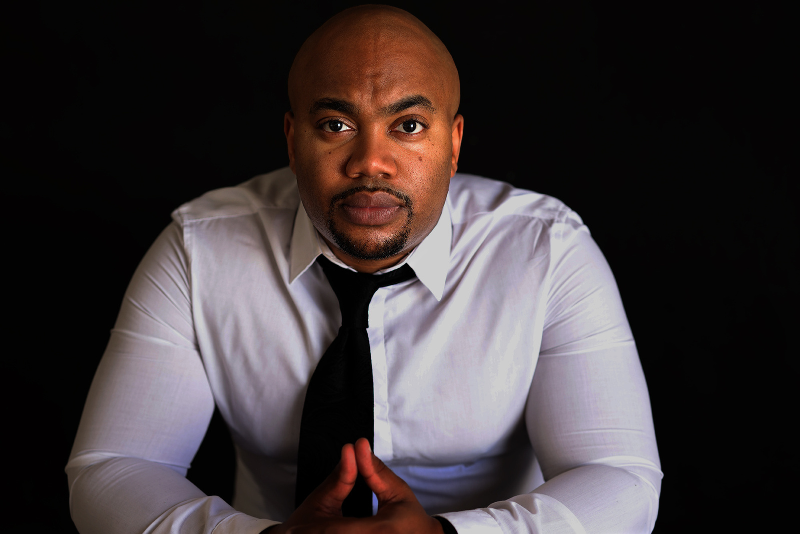 In studio headshot of professional black man in a white dress shirt and black background