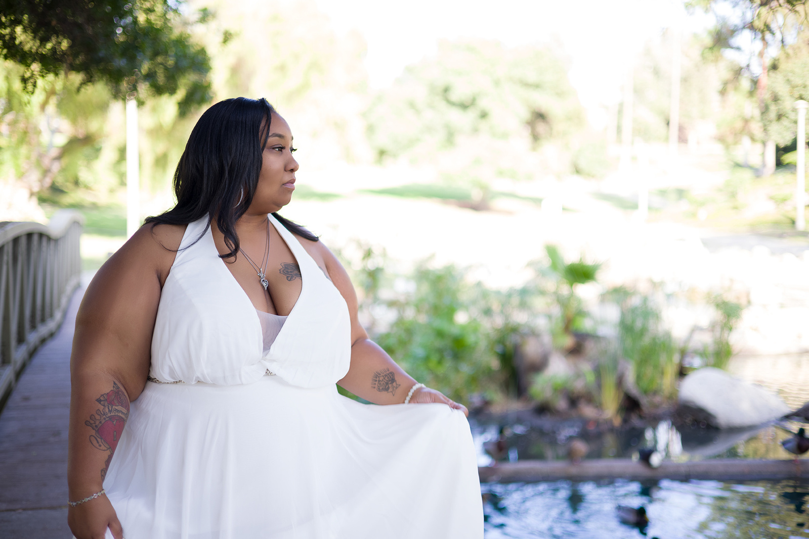 An outdoor individual portrait of a curvy black woman in a white dress looking over water in Eisenhower Park, CA
