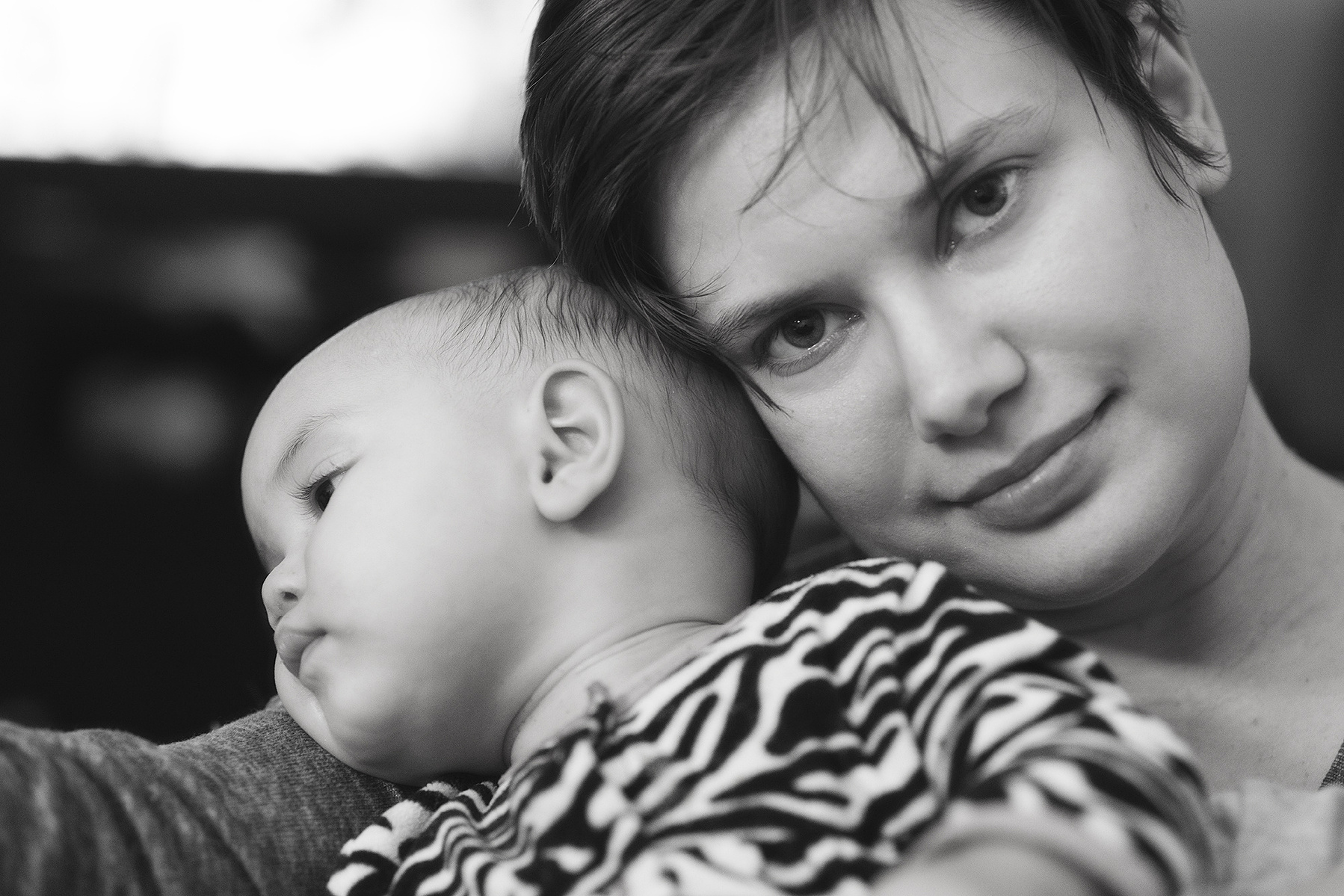 Black and white portrait of myself, a white mom with a short pixie cut in pajamas, holding my mixed nine month old daughter who is wearing a zebra print onsie.