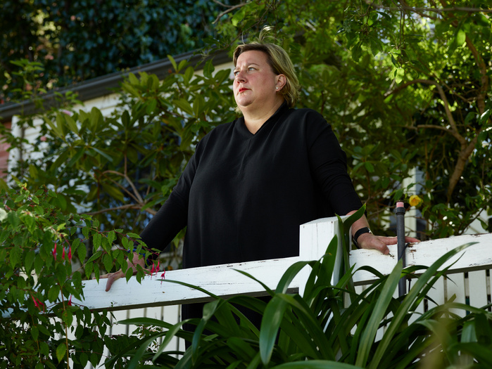 Palliative care nurse Anna Nichols looking away from camera, leaning against a handrail surrounded by garden trees.