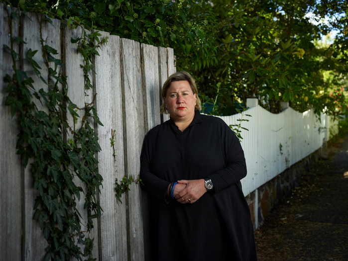 Palliative care nurse Anna Nichols in black clothing pensively leaning against a garden fence in Hobart.