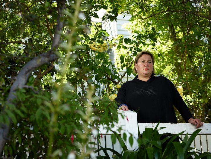 Palliative care nurse Anna Nichols looking to camera, leaning against a handrail surrounded by garden trees.