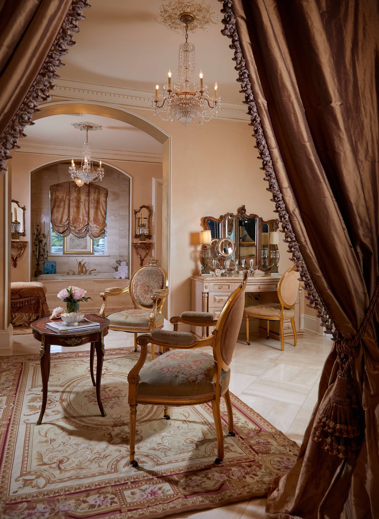 A sophisticated master bedroom with an ornate chandelier, classic decor, and luxurious furnishings, embodying timeless elegance.