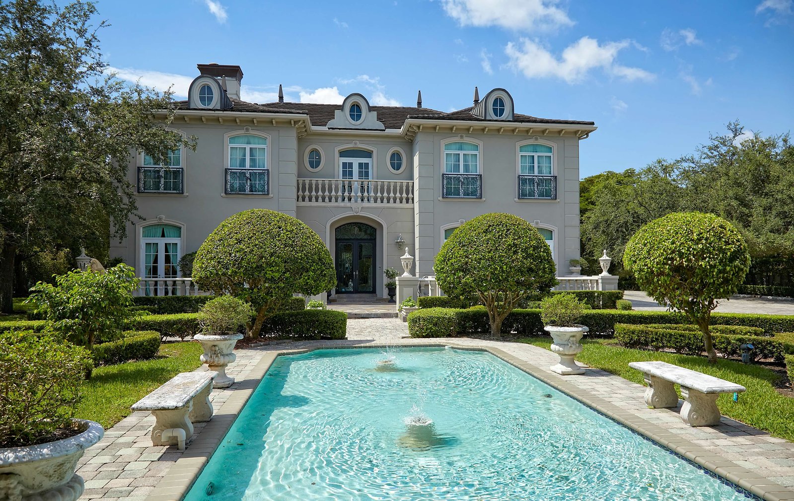 A timeless French-inspired façade framed by manicured gardens and a tranquil reflecting pool