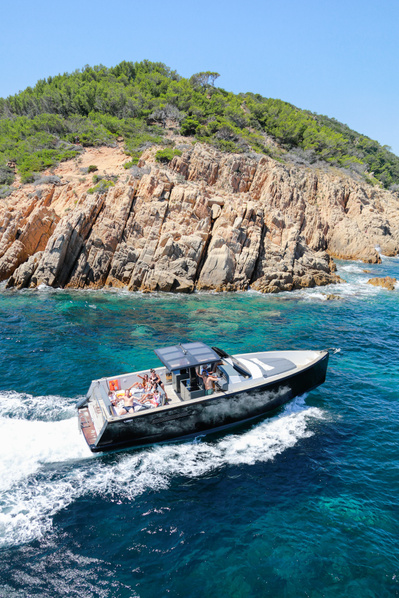 Aerial view from helicopter of a yacht in Saint-Tropez, South of France passing through rocks on turquoise water.