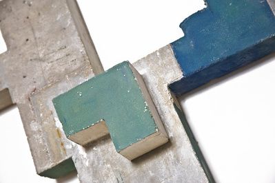 A detail of a monochromatic architectonic cubic sculpture made of cast concrete with white plaster that seems to grow organically with a bit of color