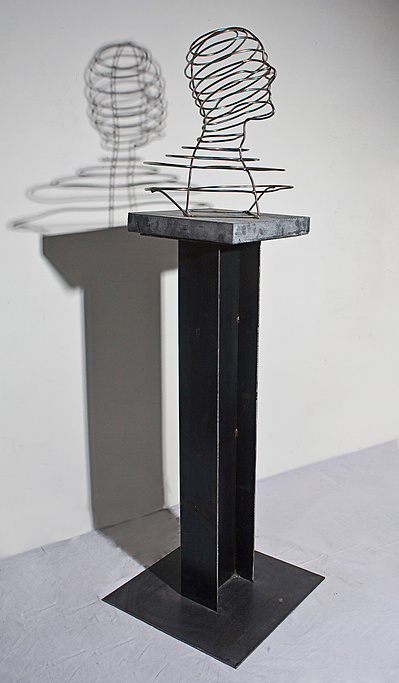 A sculpture of a full scale man's bust made of stainless steel rods seated on a pedestal. The pedestal is an I-beam using in building construction.