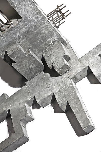 A dark monochromatic architectonic cubic sculpture made of cast concrete with white plaster that seems to grow organically from a corner up a wall and across the floor. Stainless steel is part of the construction.