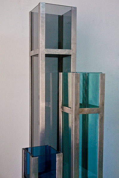 An architectonic cubic sculpture made of blue, green and brown glass and stainless steel.