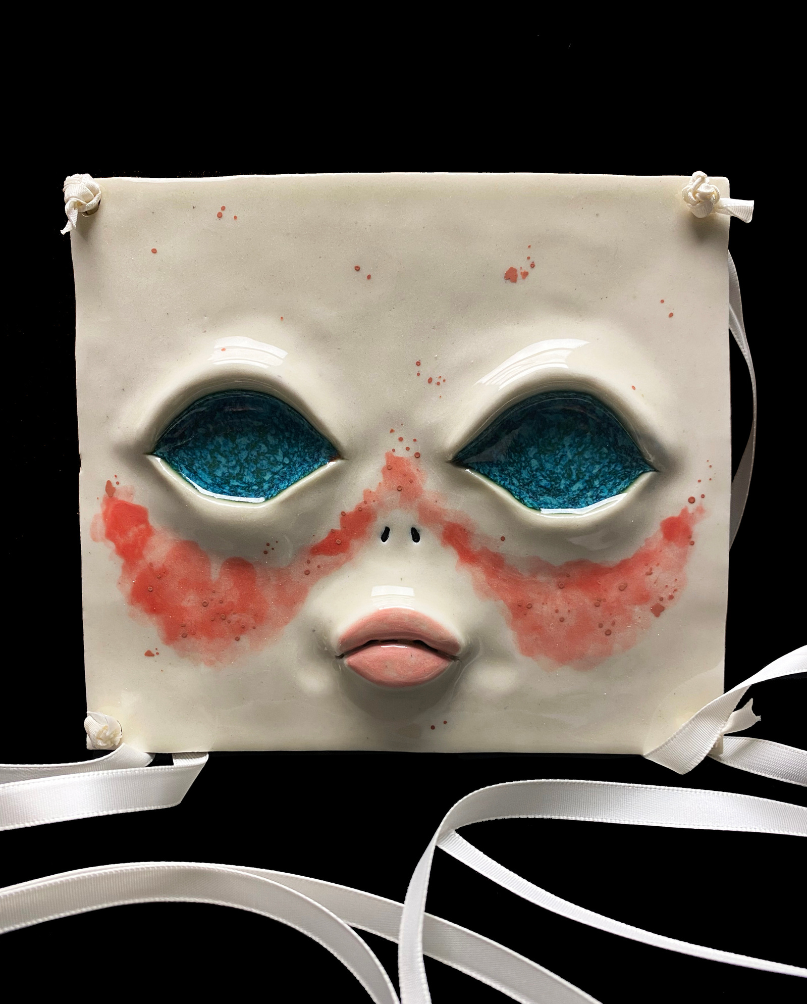 A ceramic face mask using ribbon as the strings. Bright blue iridescent eyes with pouty lips and blush.
