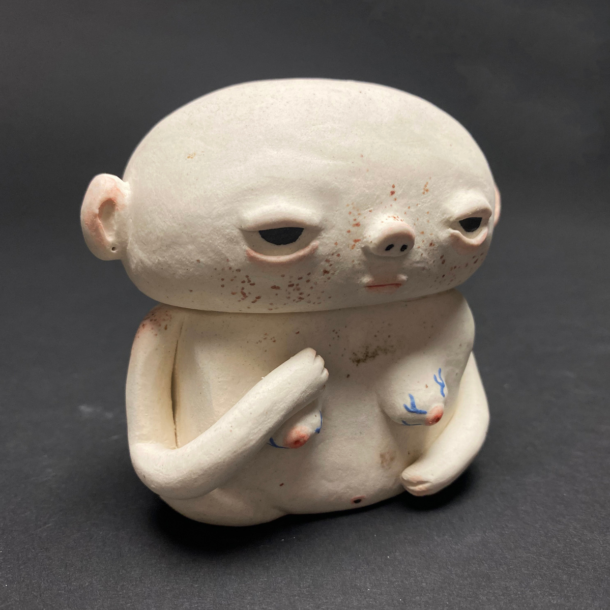 A small ceramic bust. Pale with blushed ears and shoulders, arms draped over the breast and stomach.
