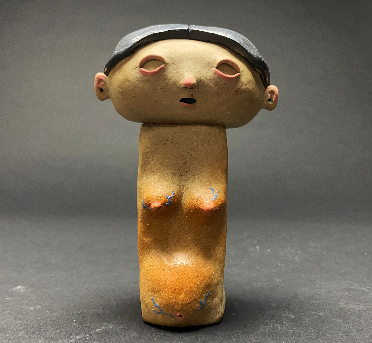 A small ceramic figure bust. A pregnant woman with blue veins trailing her stomach and breast. her mouth is slightly agape, and her black hair is in a bun with a blue scrunchie.