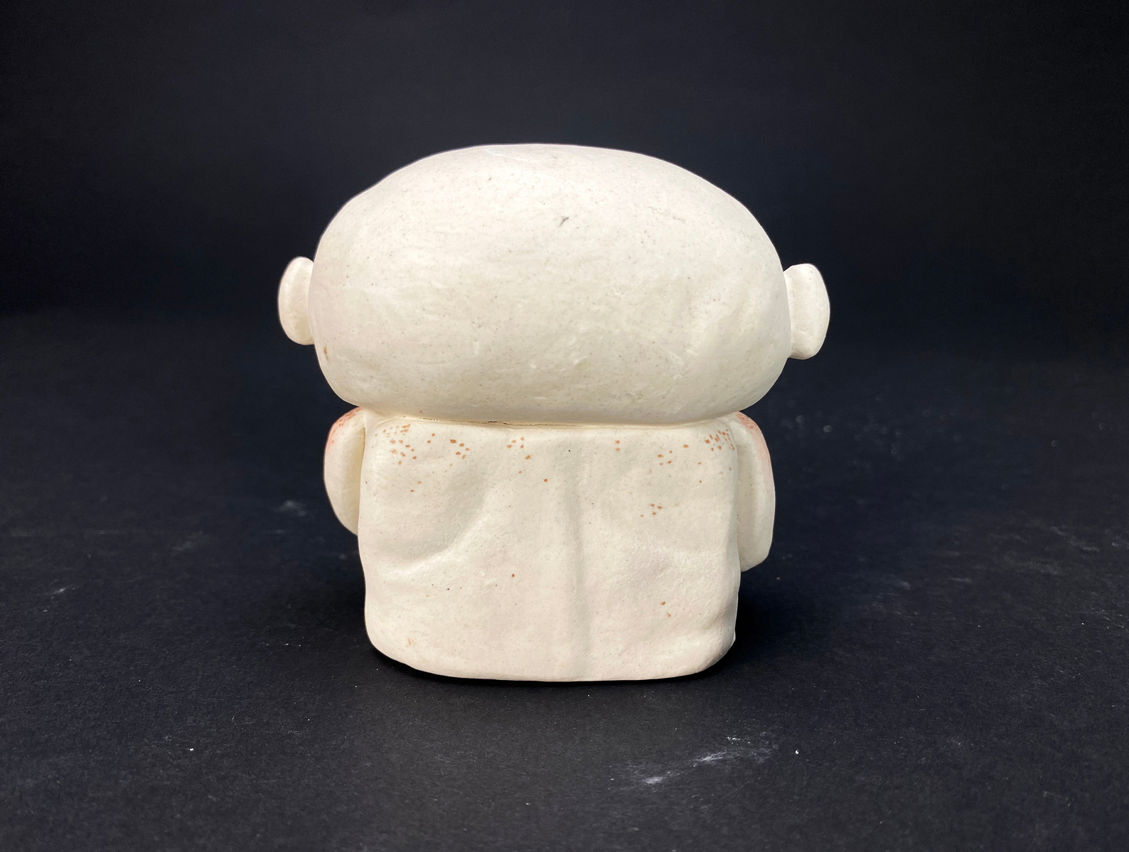 A small ceramic bust. Pale with blushed ears and shoulders, arms draped over the breast and stomach.