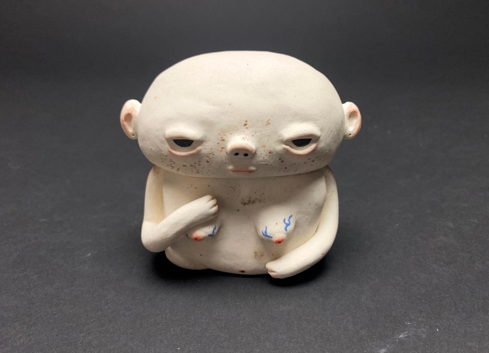 A small ceramic bust. Pale with blushed ears and shoulders, arms draped over the breast and stomach.