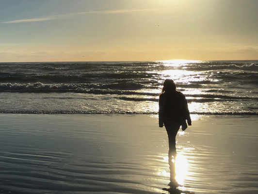 Human along coastline in direct sunlight in Cannon Beach, Oregon, highlighting contrast between foreground and background