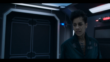 Actor stands in the corridor of a spaceship in front of an elevator door. The door has angular trim, and stylised panels.