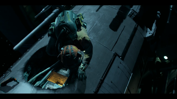 Actor in a spacesuit stands over hole which has been cut in the strut of a giant satellite. 
