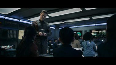 The teacher talks to a student while confiscating a small robot. There is a lighting all around the top of the walls, as well as dropped lighting panels in the ceiling. 
