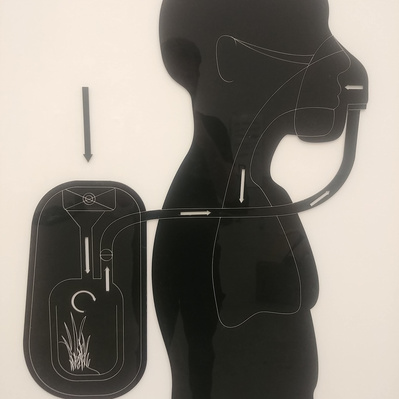 Laser cut acrylic silhouette of a person wearing a backpack. There are arrows cut and etched into the acrylic to show the direction of the air through the backpack device, and then onto the person.