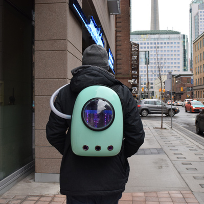 Man walks down the street facing away. He wears a backpack device which has glowing lights seen through a window.