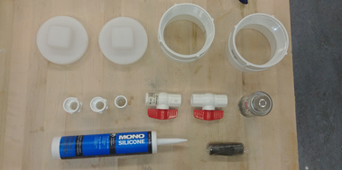 Top-down view of some of the components on a table. Including pipe caps, threaded ends, ball stop valves, thread maker, adhesive and silicone.