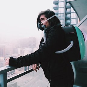 Woman wearing backpack device with mask stands on a balcony overlooking a fog-covered city