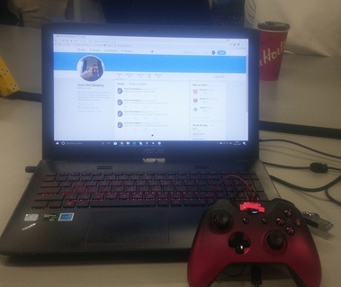 A laptop showing the screen of a twitter page called 'Sean's Not Studying'. The laptop is behind a black and pink controller. 