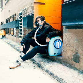 Woman sits on a step in an alley. She wears the backpack device with mask. 