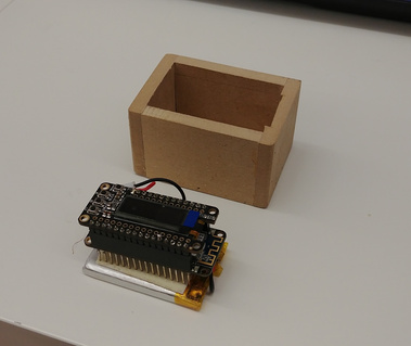 Small wooden box without the lid, next to it sits the LED screen, which is wired into a microcontroller below. which sits atop a battery.