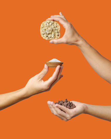 Three hands in frame holding sea salt and chocolate chip cookie and relevant ingredients. Orange background. Image shot by Megan Morello, San Diego and Southern California Food and Photographer.