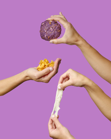 Four hands in frame holding Taro, corn flake, + mochi cookie and relevant ingredients. Purple  background. Image shot by Megan Morello, San Diego and Southern California Food and Photographer.