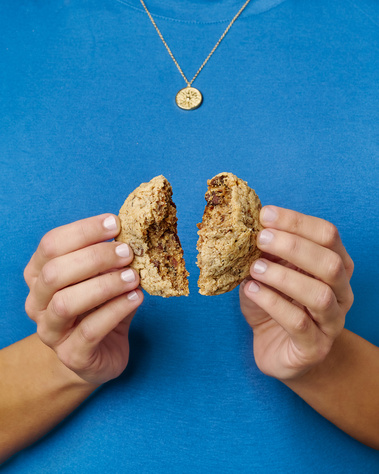 Woman wearing a blue sweater and a delicate gold necklace. Her hands are splitting a cookie in half so the croissant pieces on the inside can be seen. Image shot by Megan Morello, San Diego and Southern California Food and Photographer.